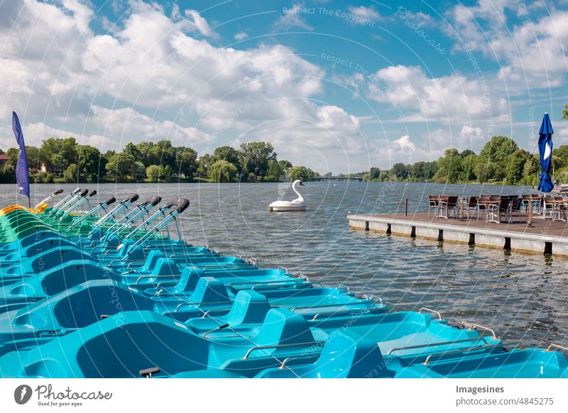 Farbige Tretboote an einem Holzsteg an einem See. Gruppe von bunten Tretbooten neben dem Holzsteg des Sees. Schwan Tretboot auf dem Aasee in Münster, Deutschland