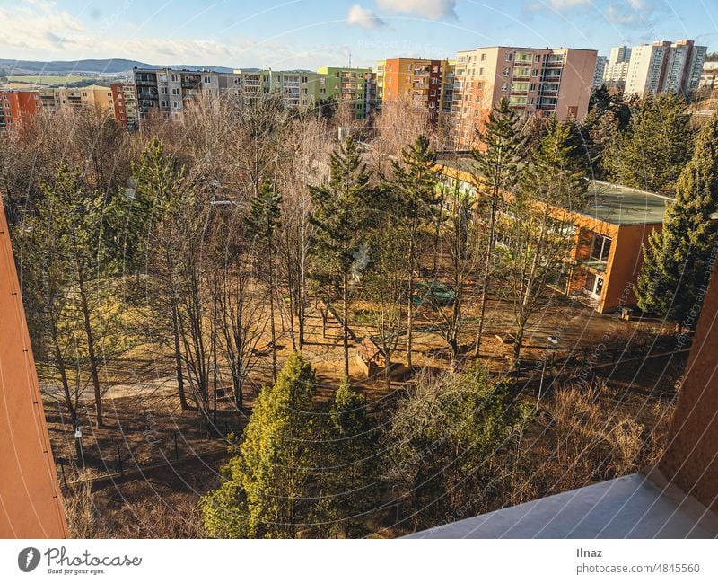 Blick aus einem Fenster auf einen Spielplatz und einen Kindergarten mit vielen Bäumen und Häusern im Hintergrund Natur Fensterblick Frühling Sommer Herbst