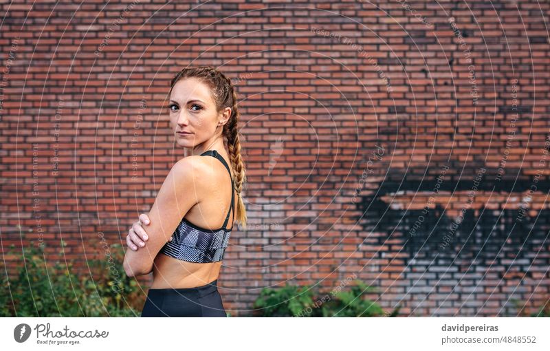 Sportlerin mit Boxerzöpfen in Pose Backsteinwand schauende Kamera seitwärts Textfreiraum Boxerflechten Taille hoch attraktiv Ermächtigung Wand Erwachsener Top