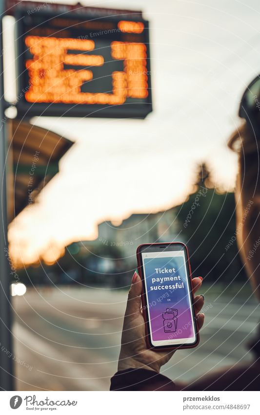 Frau kauft Fahrkarte online an der Bushaltestelle vor der Fahrt. Person, die für ein Ticket mit einer mobilen Zahlungs-App bezahlt. Technologie unterwegs nutzen. Auftragsbestätigung auf dem Handy-Bildschirm