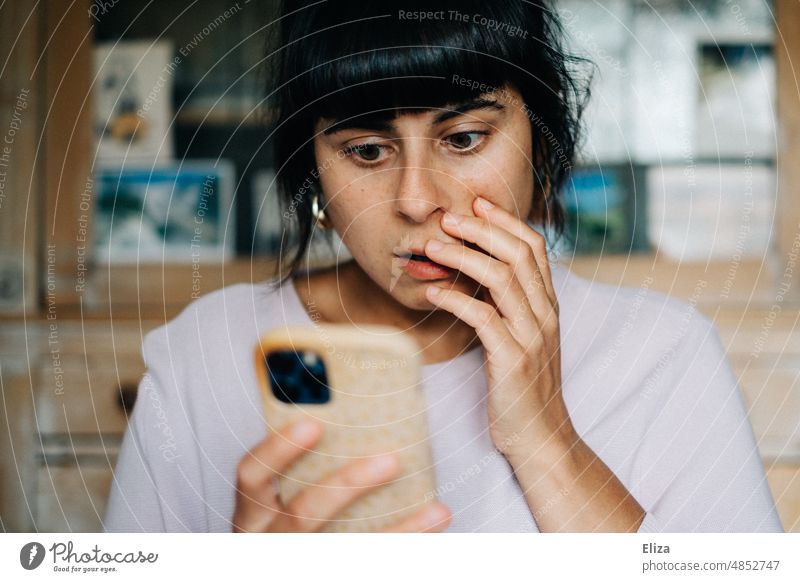 Junge Frau guckt auf ihr Smartphone und ist geschockt Schock schlechte Nachrichten Schrecken Verzweiflung Angst Panik Entsetzen Handy erschrecken börsencrash