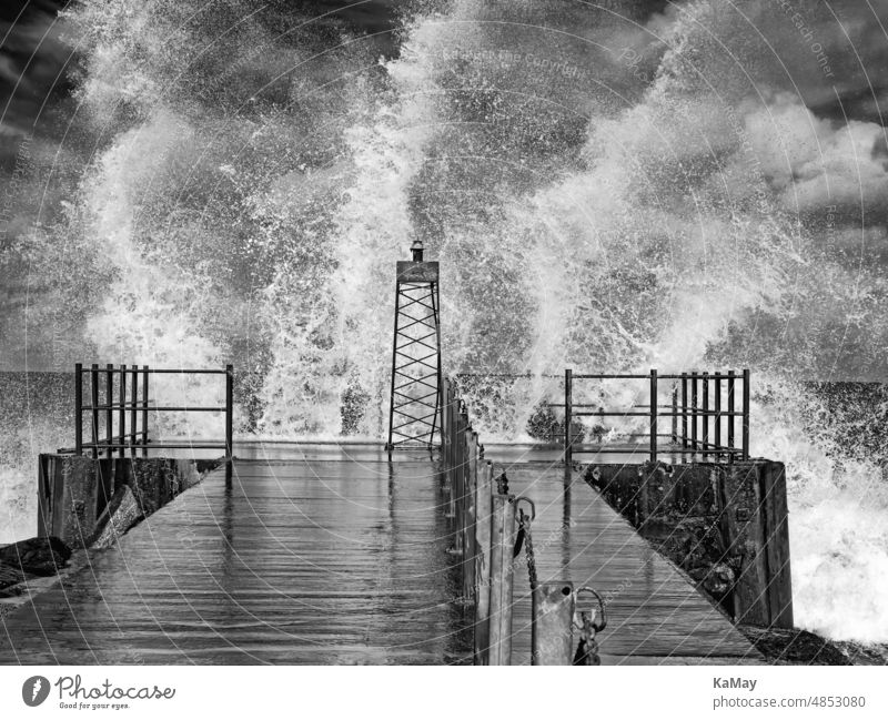 Schwarzweiße Aufnahme eines Leuchtturms bei Seegang mit aufspritzenden Wellen an der dänischen Nordseeküste von Vorupør Sturm Wetter Orkan Mole Pier Küste Meer