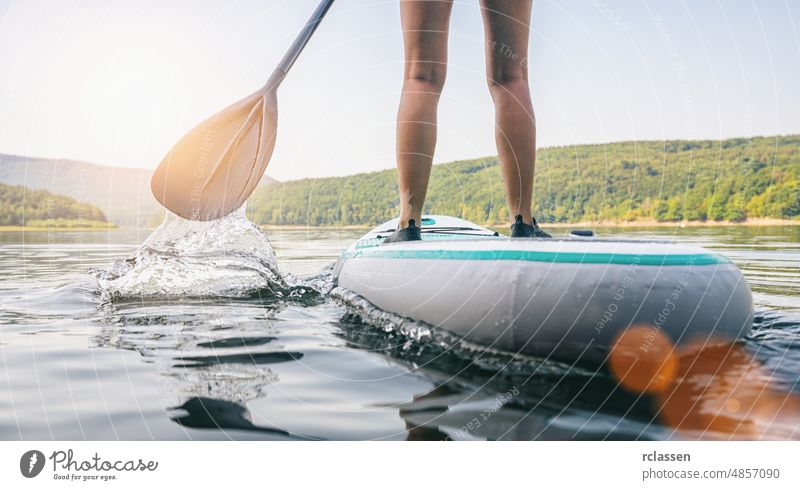 Stand Up Paddle Boarding auf einem ruhigen See im Sommer, Nahaufnahme der Beine Paddel Holzplatte stehen nach oben Paddelbrett Sport Wasser Abenteuer SUP Frau