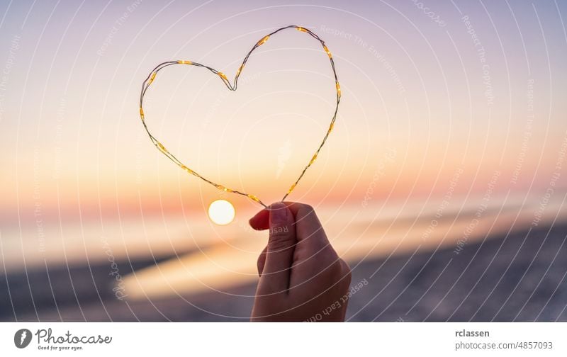 Frau hält Herzform von led Lichter am Strand bei Sonnenuntergang gemacht Leuchtdiode Liebe Hand Hintergrund Textfreiraum Sommer abstrakt Beteiligung Kunst MEER