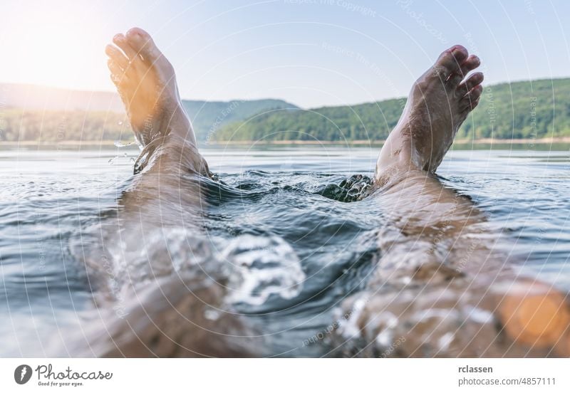 Glücklicher Mann, der sich amüsiert und mit seinen Füßen auf einem See Wasser spritzt Spaß Fuß Sommer reisen Kühlung Natur Dip Feiertag außerhalb Teich MEER