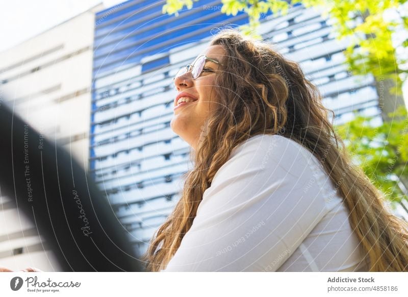 Fröhliche Frau auf der Straße sitzend Gebäude Großstadt Vorschein Stil urban feminin Lächeln Brille Haus froh Wand Stadt Sommer Dame positiv heiter Freude Glück