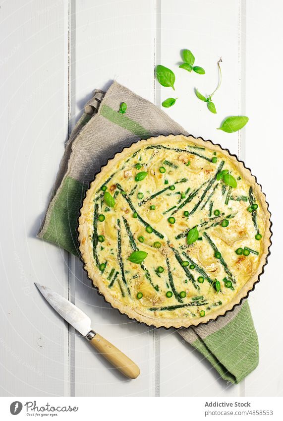 Eine Quiche mit Basilikumblättern auf dem Holztisch Sahne Bohnenkraut geschmackvoll backen französisches Essen Gesundheit Frühling Draufsicht Blatt gebacken