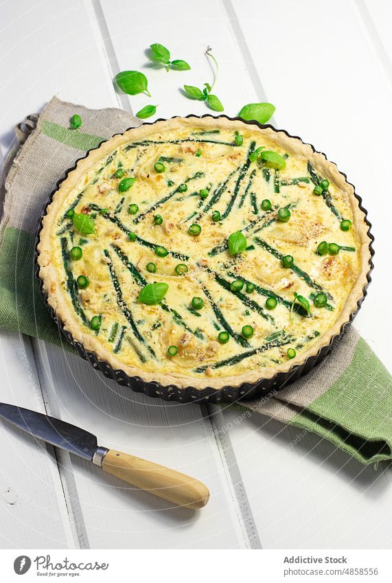 Eine Quiche mit Basilikumblättern auf dem Holztisch Sahne Bohnenkraut geschmackvoll backen französisches Essen Gesundheit Frühling Draufsicht Blatt gebacken