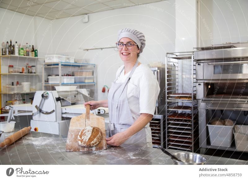 Zufriedener Bäcker mit frischem Brot Frau gebacken Brotlaib kulinarisch Bäckerei Küche Gastronomie Industrie unordentlich Licht Tisch Schneidebrett Vorrichtung