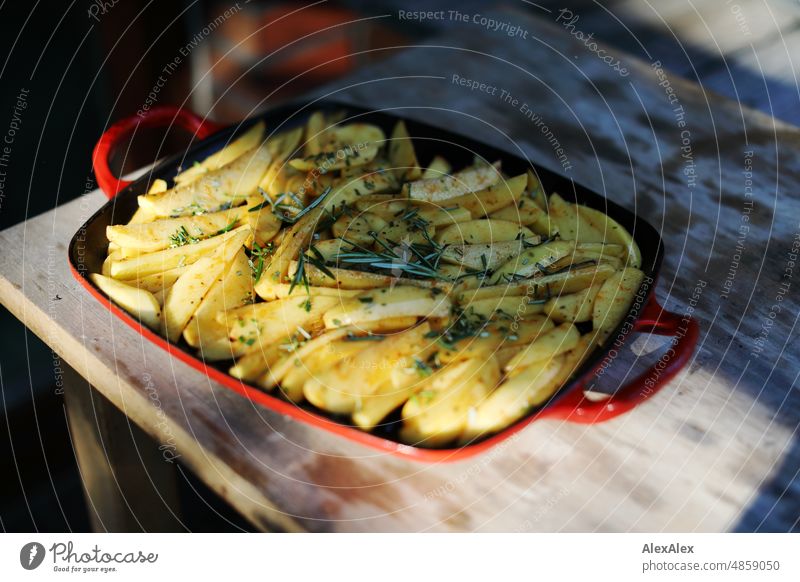 Kartoffelspalten und Rosmarin in einer roten Grillpfanne auf einem Holztisch - Sonnenuntergang, Abend, Sommer Kartoffeln Pommes Fites Rosmarion Essen Food