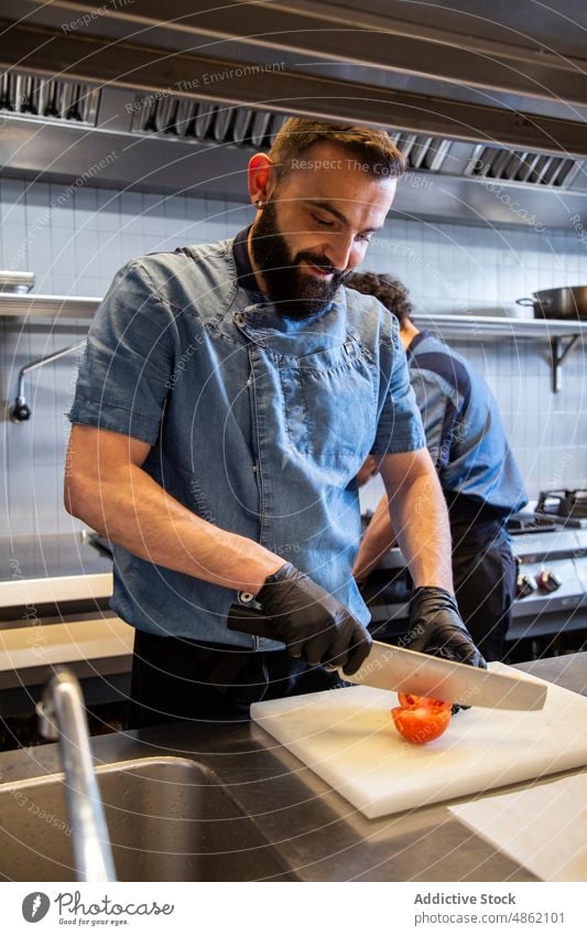 Koch schneidet Tomate auf Schneidebrett im Restaurant Küchenchef Schneiden Holzplatte Essen zubereiten vorbereitend Lebensmittel Messer Gemüse Mahlzeit