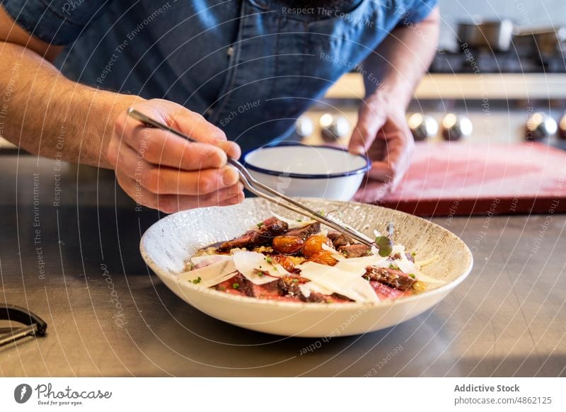 Chefkoch beim Garnieren von Kräutern auf Hauptgericht in Großküche Küchenchef Garnierung Kraut Main Speise Pinzette Abfertigungsschalter wirtschaftlich Steak