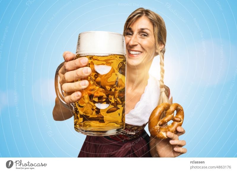 Junge sexy traditionelle Oktoberfest-Besucherin in traditioneller bayerischer Tracht, die einen großen Bierkrug und eine Brezel auf blauem Hintergrund hält