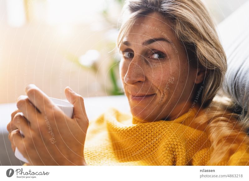 Frau sitzt auf der Couch mit einer Tasse in den Händen und lächelt, während sie vor sich hinschaut, Entspannungskonzeptbild Kaffee trinken Sofa sitzen heimwärts