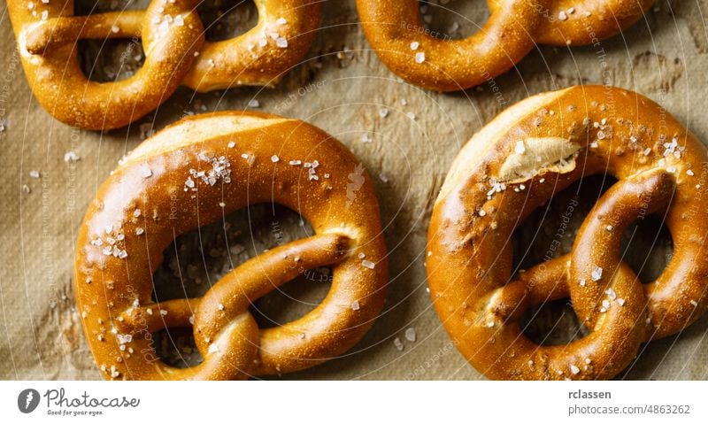 Bayerisch leckere, frisch gebackene und frisch zubereitete, hausgemachte weiche Brezel auf Backpapier liegend, bereit für das Oktoberfest Deutsch bayerisch