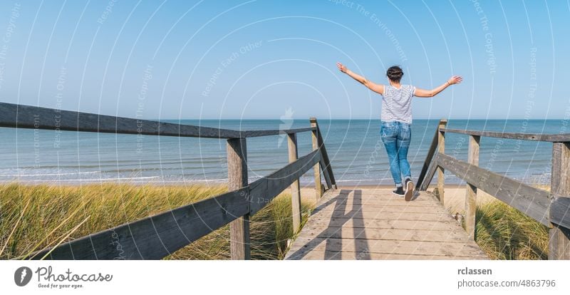 Frau hebt die Hände auf einem hölzernen Weg zur Ostsee über Sanddünen Strand Laufsteg angehoben Promenade reisen Abenteuer Effizienz Energie baltisch Nordsee