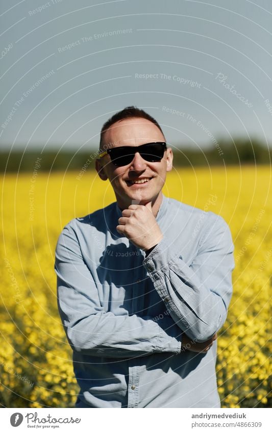 Ein junger Mann mit Sonnenbrille geht spazieren und amüsiert sich über ein sonniges gelbes Rapsfeld, das Konzept von Reisen und Freiheit. Sommerurlaubshintergrund