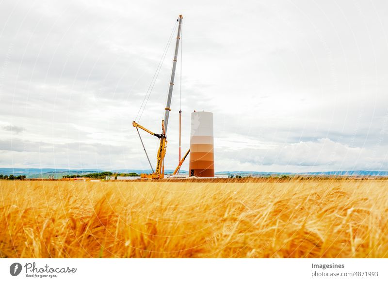 Bau und Montage einer Windkraftanlage per Kran auf einer Baustelle. Ackerland mit Bauarbeiten am Windpark in Deutschland. Energiesparkonzept aus dem Bau von Windkraftanlagen mit Wolkenhimmel