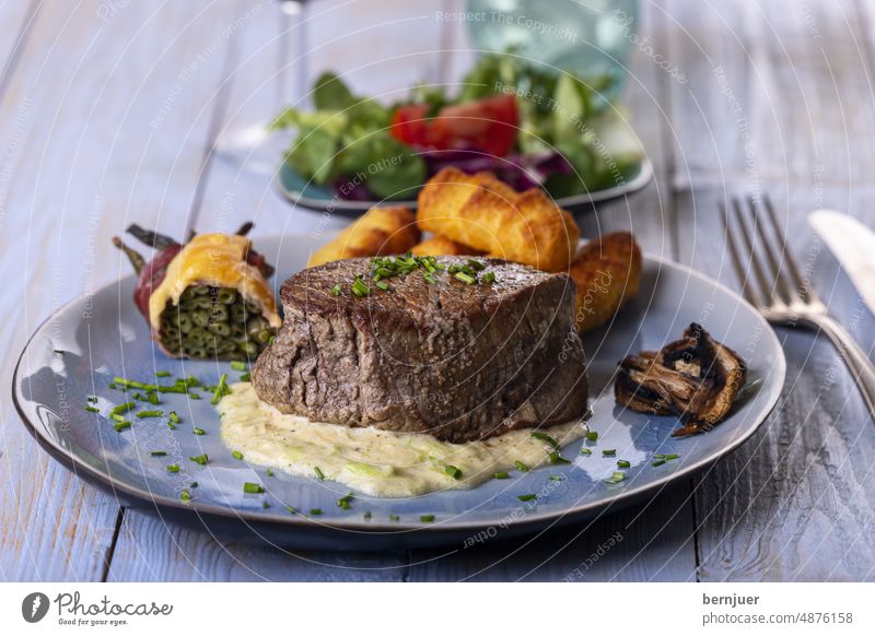 Nahaufnahme eines Steaks auf einem Teller Rindersteak Holz Rindssteak Rindfleisch Filet Portion Blau Wasser Rot Wein rustikal Pilz Speck Käse Bohnen