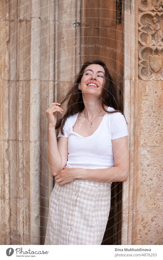 Junge Touristin posiert in der Nähe der alten Kathedrale. Neutrale Farben in der Kleidung Stil. Beige Farbe Wände. Frau Tourist trägt weißes T-Shirt. Sommer