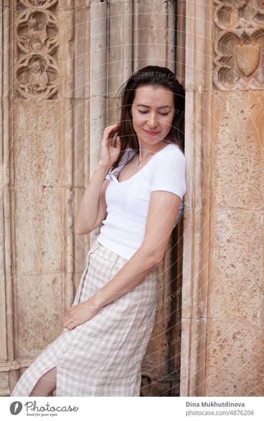 Junge Touristin posiert in der Nähe der alten Kathedrale. Neutrale Farben in der Kleidung Stil. Beige Farbe Wände. Frau Tourist trägt weißes T-Shirt. Sommer