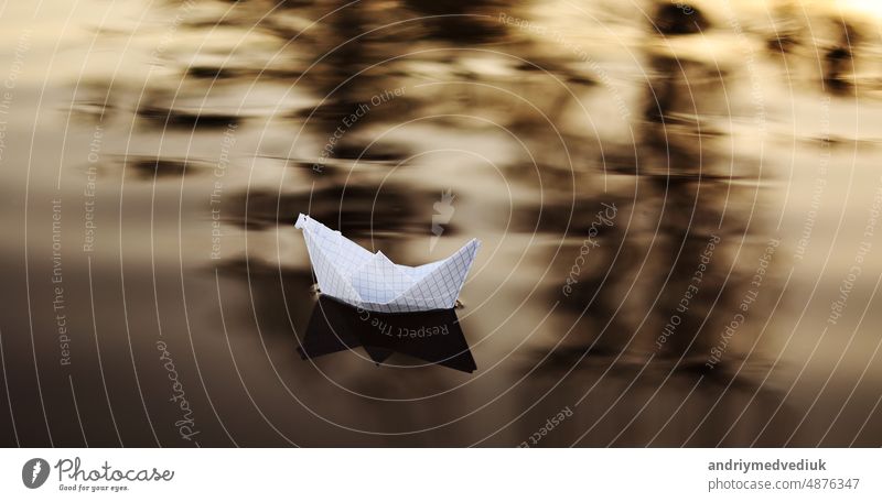 Ein Papierboot schwimmt auf den Wellen im Wasser bei einem schönen Sonnenuntergang. Origami Schiff Segeln. Das Konzept eines Traums, Zukunft, Kindheit, Freiheit oder Hoffnung.