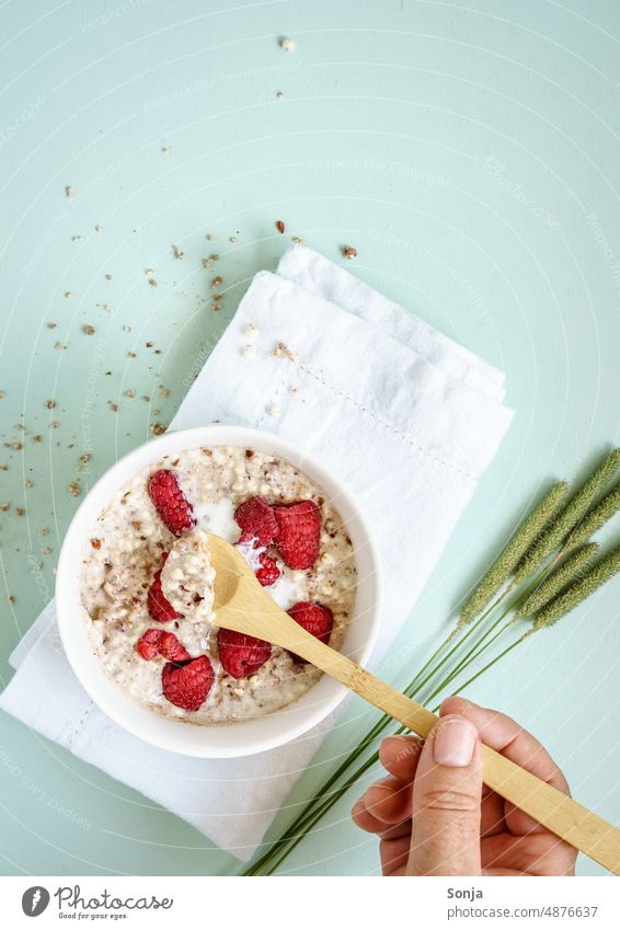 Eine Frau isst warmen Haferbrei mit Himbeeren mit einem Holzlöffel. Porridge. Frühstück Essen Milch Löffel Teilansicht Schalen & Schüsseln Gesundheit Frucht