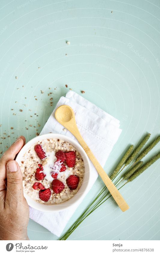 Hand hält warmen Haferbrei mit frischen Himbeeren in einer Schüssel auf einem Tisch. Porridge. Frühstück melken Schalen & Schüsseln Frau Haferflocken Löffel