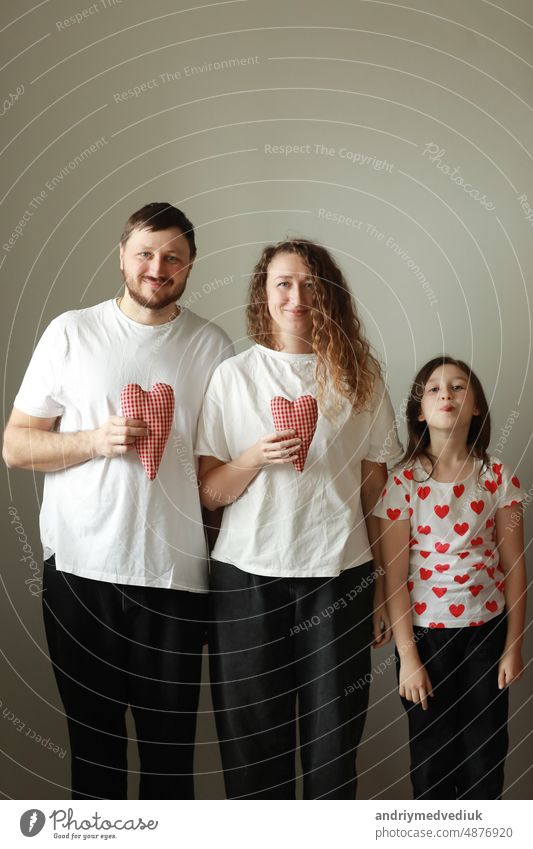 valentines tag. glückliche familie, mutter, vater und kleine tochter in weißen t-shirts halten handgemachte rote herzen in ihren händen und schauen in die kamera auf weißem hintergrund. glück, gesundheit und liebe konzept