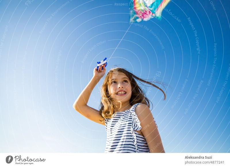 Nettes glückliches kleines Mädchen im Sommerkleid läuft mit fliegenden Drachen auf leeren Sandstrand. Schöner sonniger Tag, blauer Himmel. aktiv Aktivität