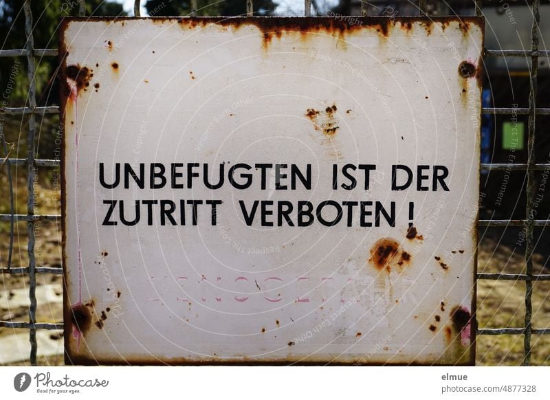 rostendes Schild mit der Aufschrift  UNBEFUGTEN IST DER ZUTRITT VERBOTEN in schwarz und  LEBENSGEFAHR in verbleichendem rot an einem Metallzaun Zutritt verboten