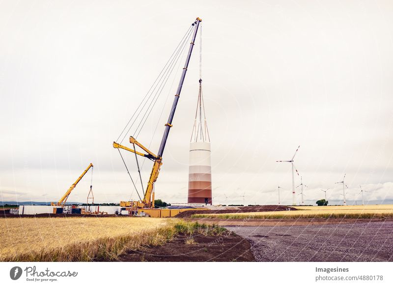 Bau und Montage einer Windkraftanlage per Kran auf einer Baustelle. Ackerland mit Bauarbeiten am Windpark in Deutschland. Energiesparkonzept aus dem Bau von Windkraftanlagen mit Wolkenhimmel