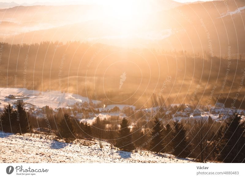 Sonnenaufgang über dem polnischen Dorf Koniakow mit dem Wald, durch den die Sonnenstrahlen im Morgennebel fallen. Ein atemberaubender Anblick an einem kalten Morgen