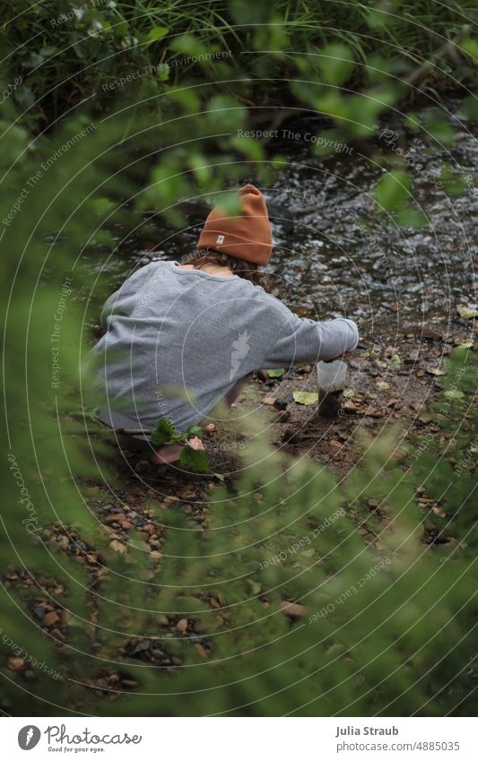 Kind spielt am Bachufer mit Steinen Kindheit Im Freien Freiheit Abenteuer nass Wasser Kieselsteine Farnblatt Blätter grün Grünpflanze Außenaufnahme natürlich