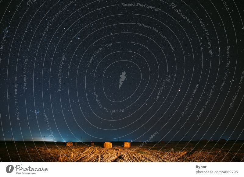 Night Starry Sky Above Haystacks In Summer Agricultural Field. Nacht Sterne über ländliche Landschaft mit Heuballen nach der Ernte. Landwirtschaftliches Konzept