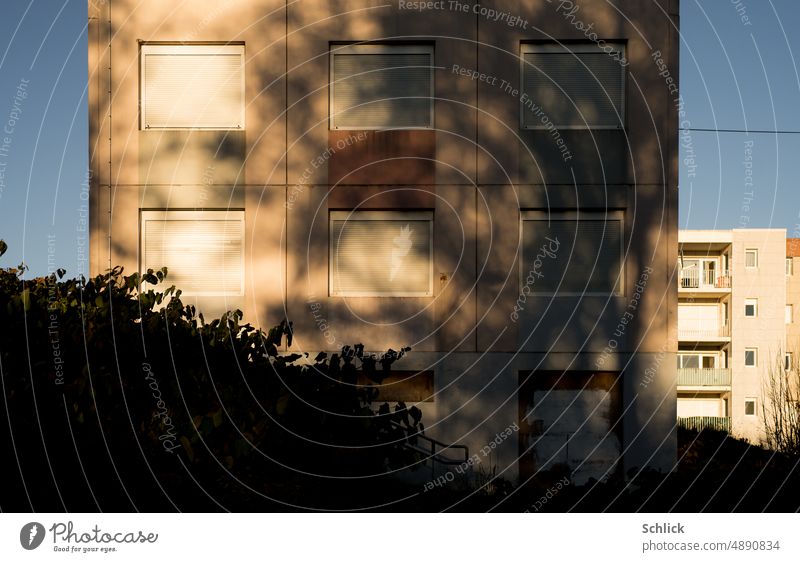 Fassaden unbewohnter Wohnblock mit Abschattung durch Baum und geschlossenen Rollläden Schatten Schattenwurf Hitze Rollladen zu quadratisch rosa schattig Himmel