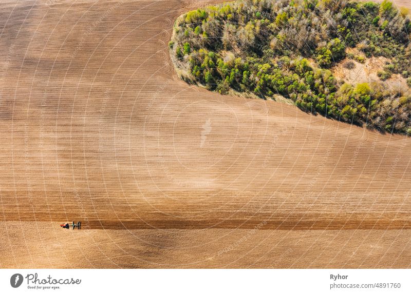 Traktor pflügt Feld im Frühling. Beginn der landwirtschaftlichen Saison. Grubber gezogen von einem Traktor in der Landschaft ländlichen Feld. Ländliches Feld Landschaft. Luftaufnahme. Top Flachansicht