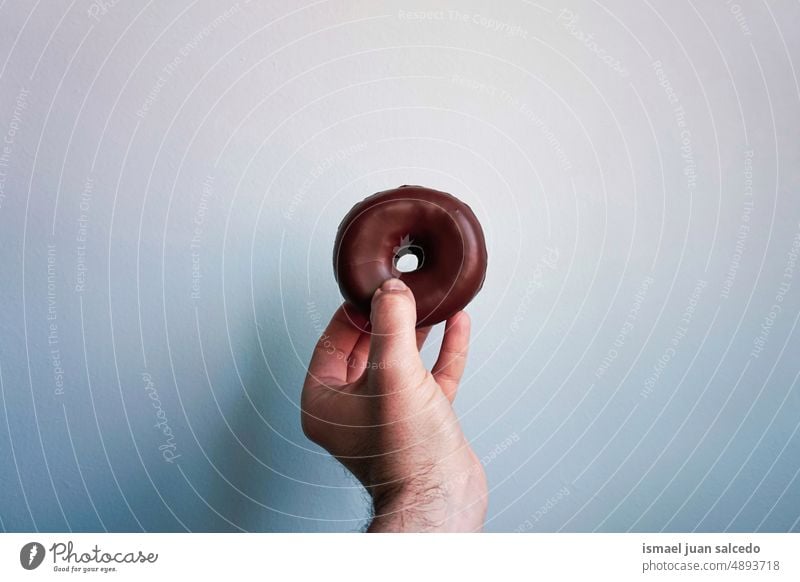 die Hand hält einen Schokoladendonut, ein leckeres, aber ungesundes Essen Doughnut Krapfen Schokoladen-Donut Lebensmittel Gebäck Frühstück Brunch Snack süß