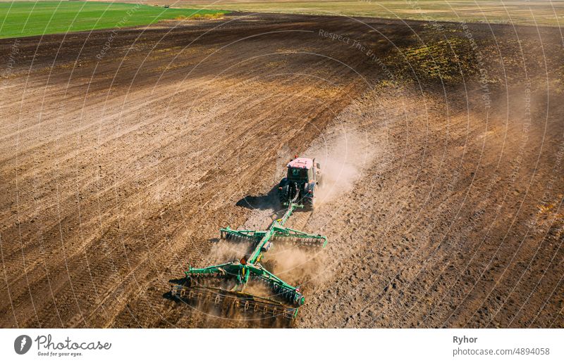 Luftaufnahme. Traktor pflügt Feld. Beginn der landwirtschaftlichen Frühjahrssaison. Cultivator Pulled By A Tractor In Countryside Rural Field Landscape. Staub steigt von unter Pflügen