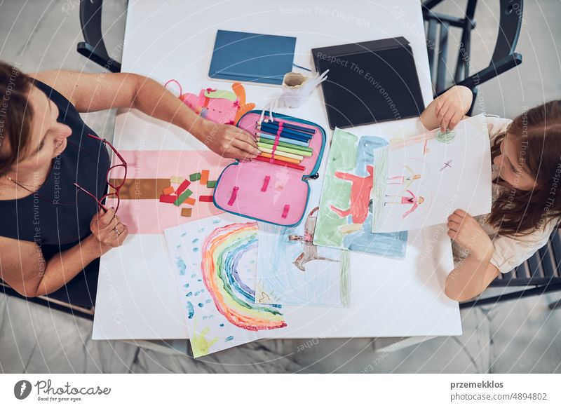 Mädchen präsentiert ihr Kunstwerk Lehrer. Frau unterstützt Schülerin während des Unterrichts in der Grundschule. Kind zeichnet Bild am Schreibtisch sitzend im Klassenzimmer. Lernen in der Grundschule. Zurück zur Schule