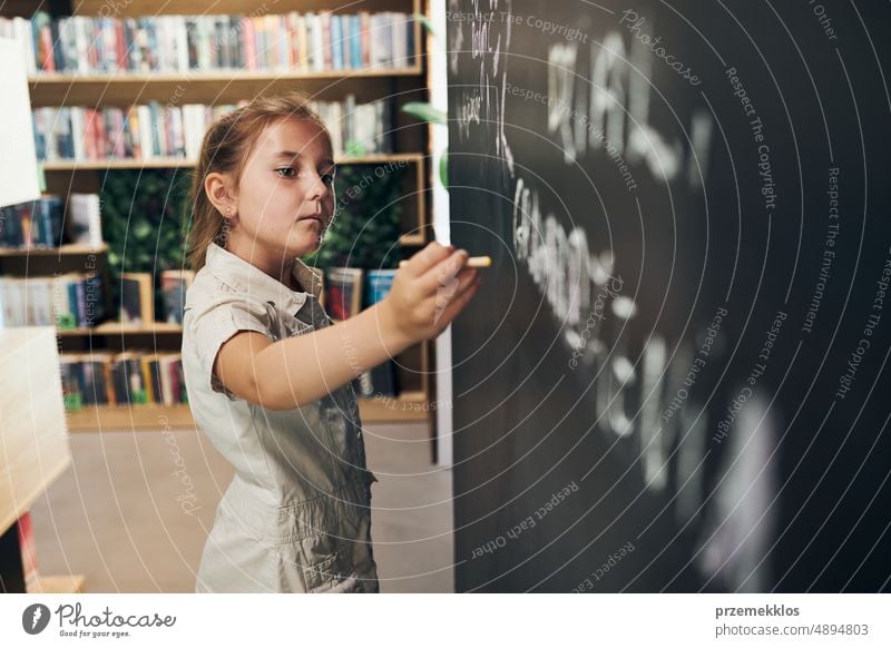 Kleines Mädchen schreibt auf Tafel. Smart Student setzen lösen auf Kreidetafel. Zurück zur Schule. Kind hat Unterricht. Schülerin lernt in der Grundschule