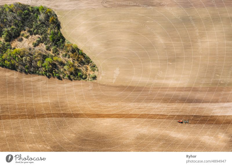 Traktor pflügt Feld im Frühling. Beginn der landwirtschaftlichen Saison. Grubber gezogen von einem Traktor in der Landschaft ländlichen Feld. Ländliches Feld Landschaft. Luftaufnahme. Top Flachansicht