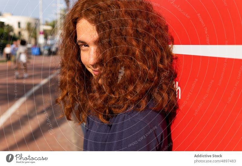 Frau mit lockigem Haar Rotschopf Behaarung schön Sonnenlicht Wand Lifestyle Arme angehoben Freizeit T-Shirt attraktiv Ausdruck Vorderansicht Kopfschuss sonnig