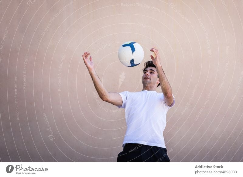 Junger männlicher Spieler beim Fußballtraining jung praktizieren Wand beige Bewegung Gericht Ball Athlet Spielen Textfreiraum Sport Fußballer Fitness Konkurrenz