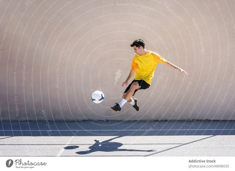 Junger männlicher Spieler beim Fußballspielen jung tretend springen Gebäude Gericht Bewegung springend Mann Gleichgewicht Tatkraft Großstadt Ball Athlet Spielen