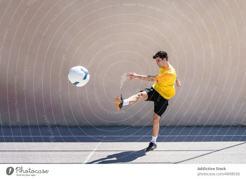 Junger männlicher Spieler beim Fußballspielen jung tretend springen Gebäude Gericht Bewegung springend Mann Gleichgewicht Tatkraft Großstadt Ball Athlet Spielen