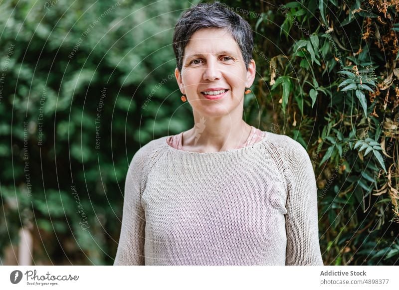 Glückliche reife Frau lächelt in die Kamera im grünen Garten Lächeln Natur Landschaft positiv froh Porträt Baum Vorschein elegant Park Lebensmitte Kurze Haare