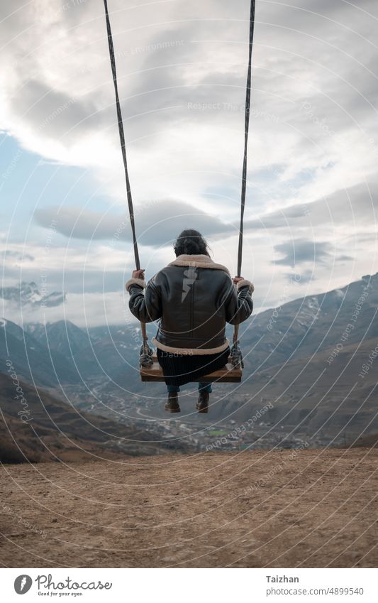 Junges Mädchen, das auf einer selbstgebauten Schaukel schaukelt Vor dem Hintergrund des bewölkten Himmels und der Berghügel pendeln Frau swinging Natur sonnig