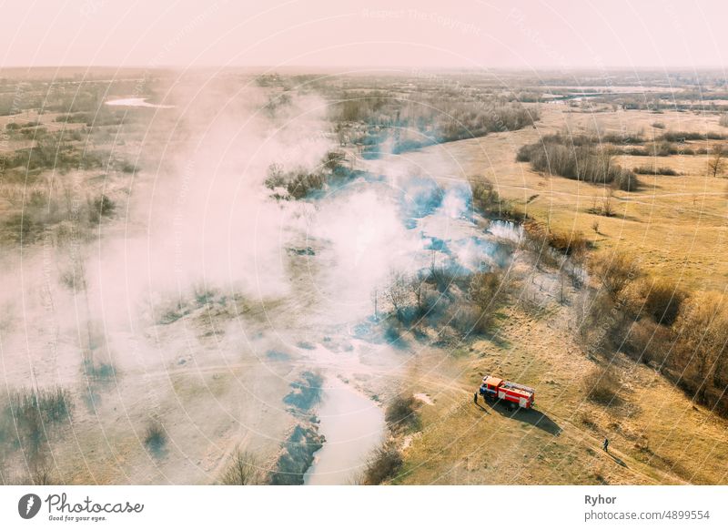 Luftaufnahme. Frühling trockenes Gras brennt während Dürre heißes Wetter. Buschfeuer und Rauch. Feuerwehrauto, Feuerwehrauto auf Brandbekämpfung Betrieb. Wildes offenes Feuer vernichtet Gras. Ökologisches Problem Luftverschmutzung