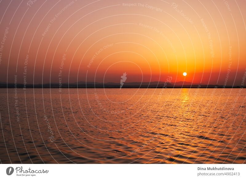 Schöner Sonnenuntergang auf dem See mit entfernten Silhouette der Berge und Sonne über dem Wasser untergehen. Orange und rote Farbe Sonnenuntergang in den Naturpark horizontale Banner.